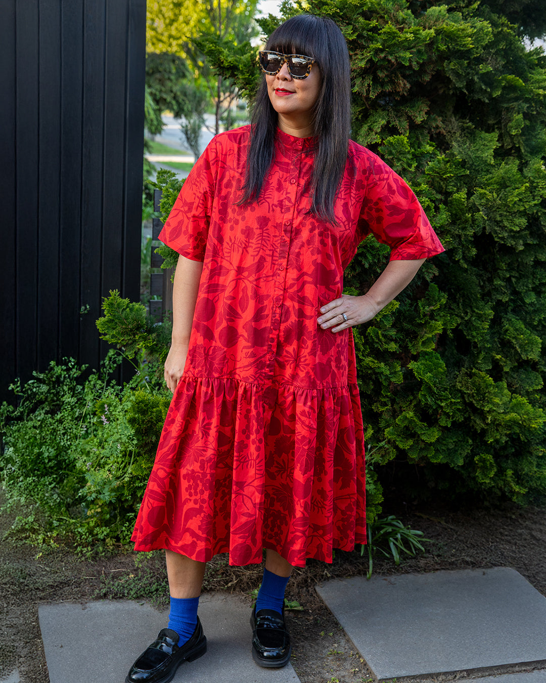 Person wearing a red dress standing outdoors with greenery in the background
