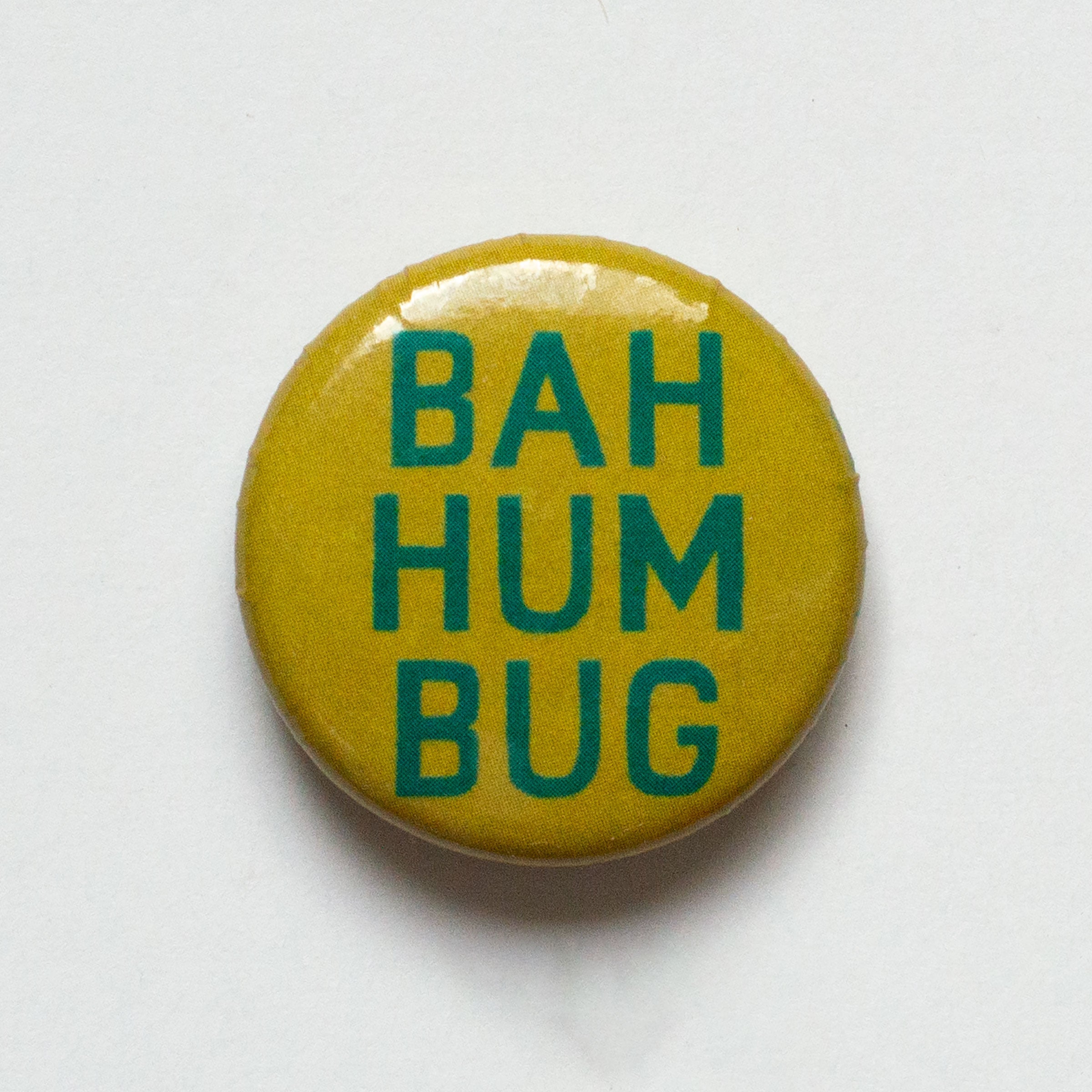 BAH HUM BUG in green text on a golden mustard background 1 inch pin