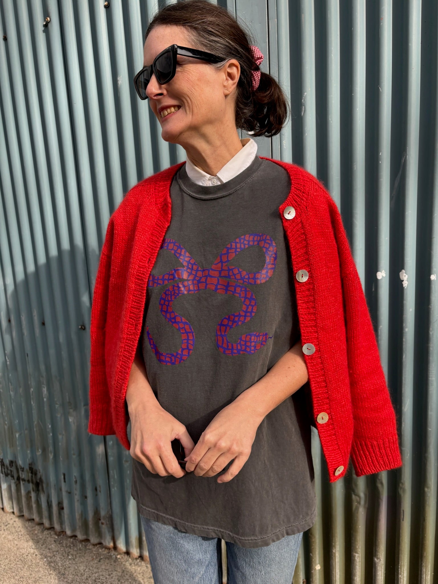 Woman wearing a snake bow graphic on a black t-shirt and red sweater against a grey wall