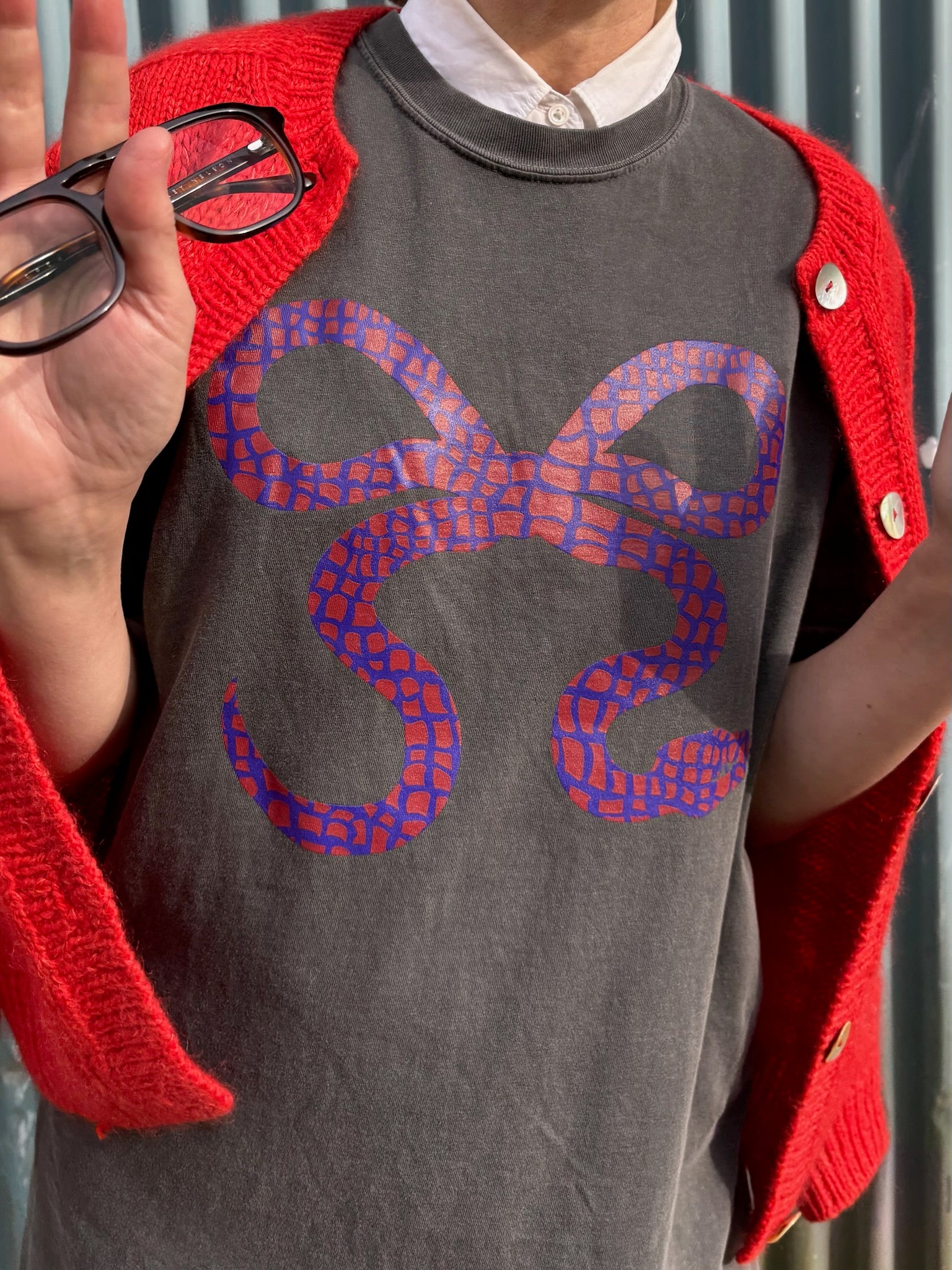 Woman wearing a snake bow graphic on a black t-shirt and red sweater against a grey wall
