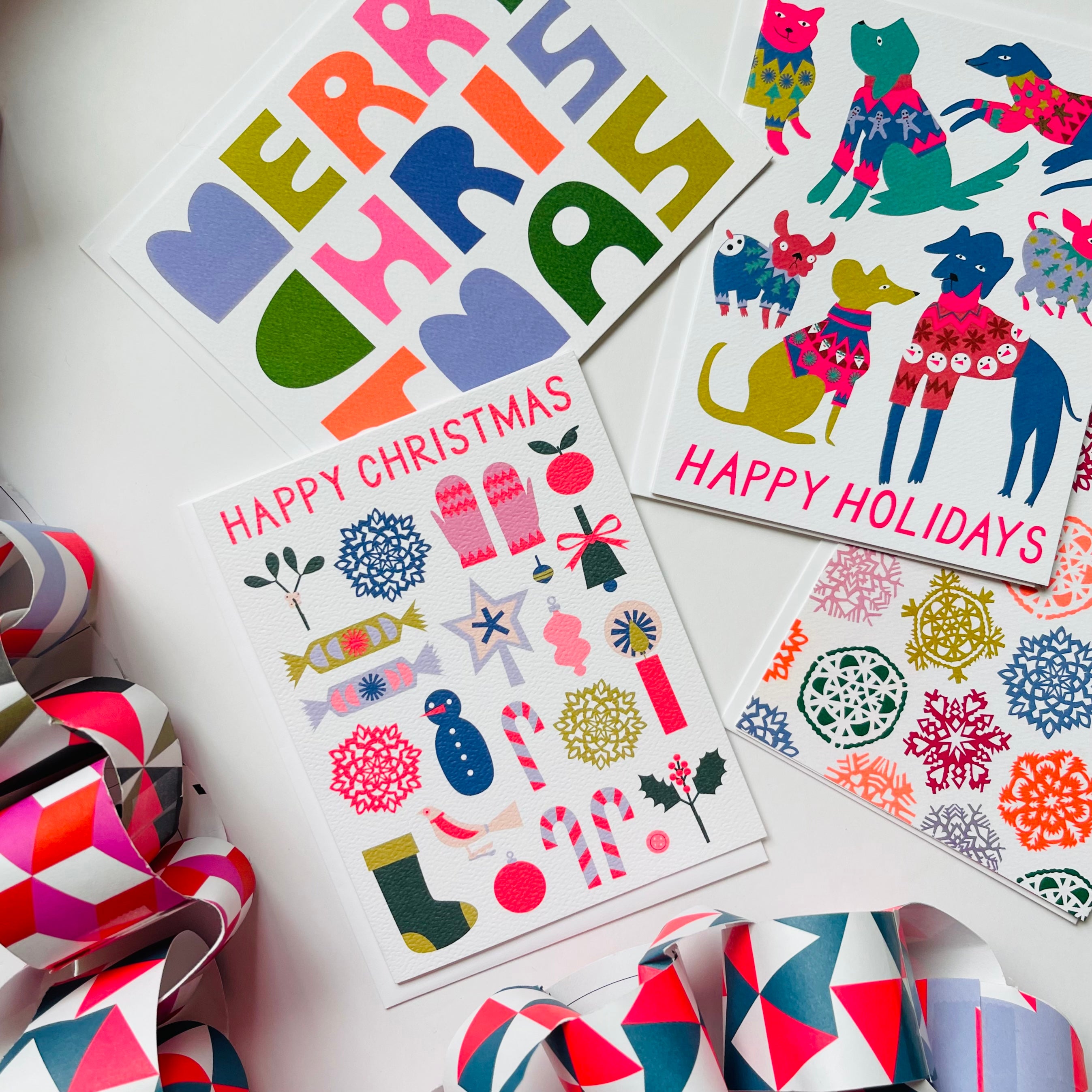 Merry Christmas Happy Holidays Happy Christmas Holiday card with multicoloured text that says Merry Christmas in a hand drawn font that has a paper block cut look