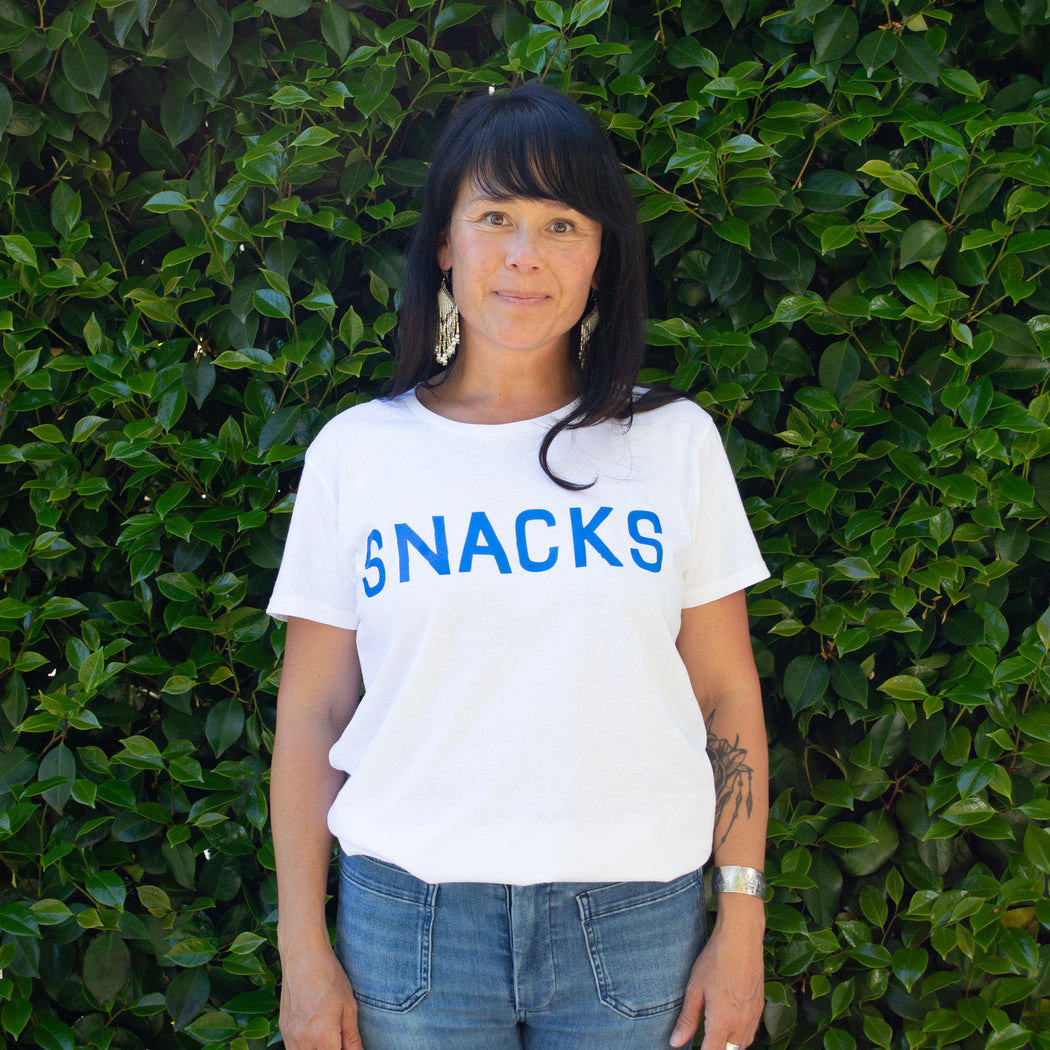 Happy model wears a basic white t-shirt screenprinted with "Snacks"