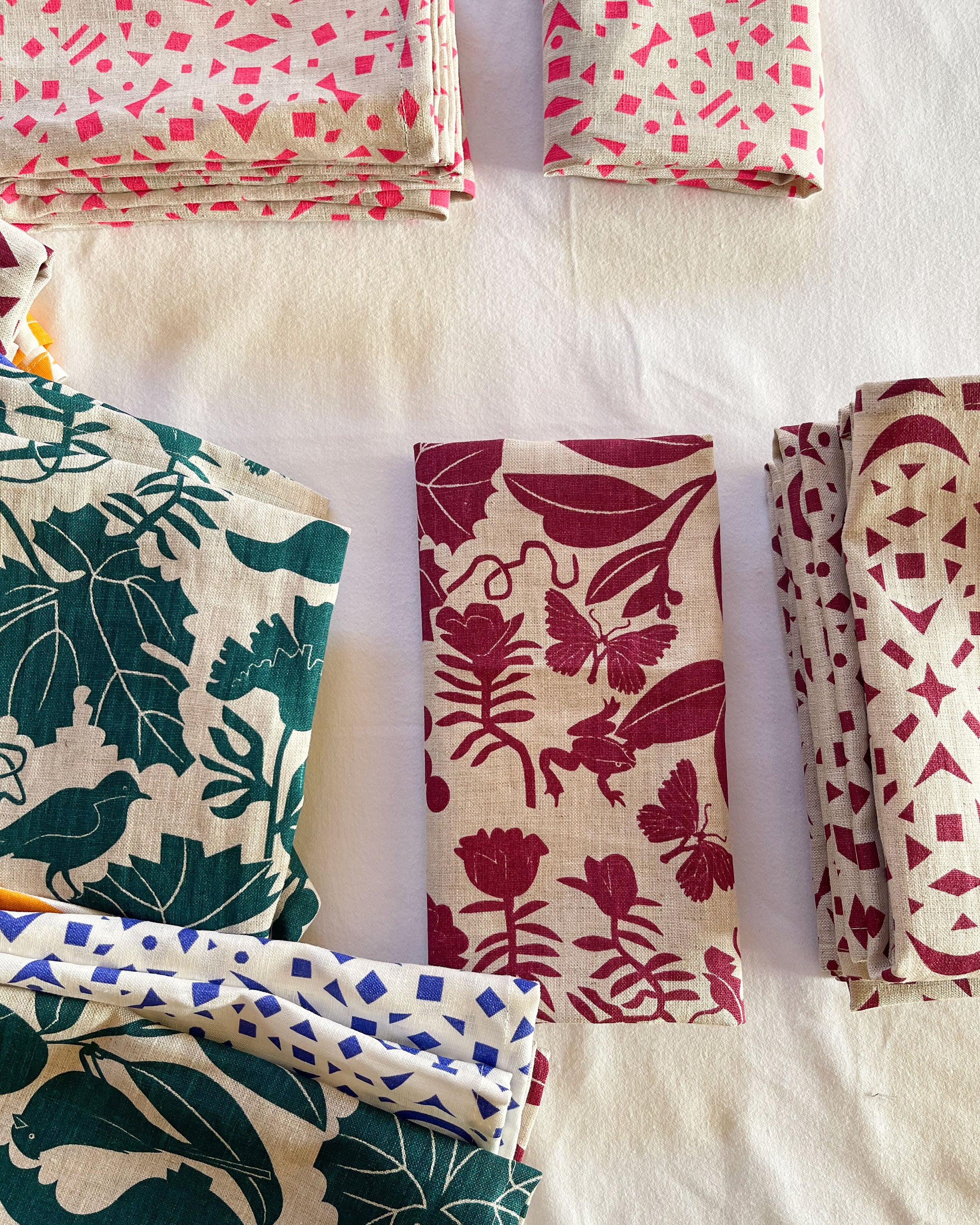 folded linens in piles California and Snowflake print in burgundy with emerald green California prin and neon pink snowflake