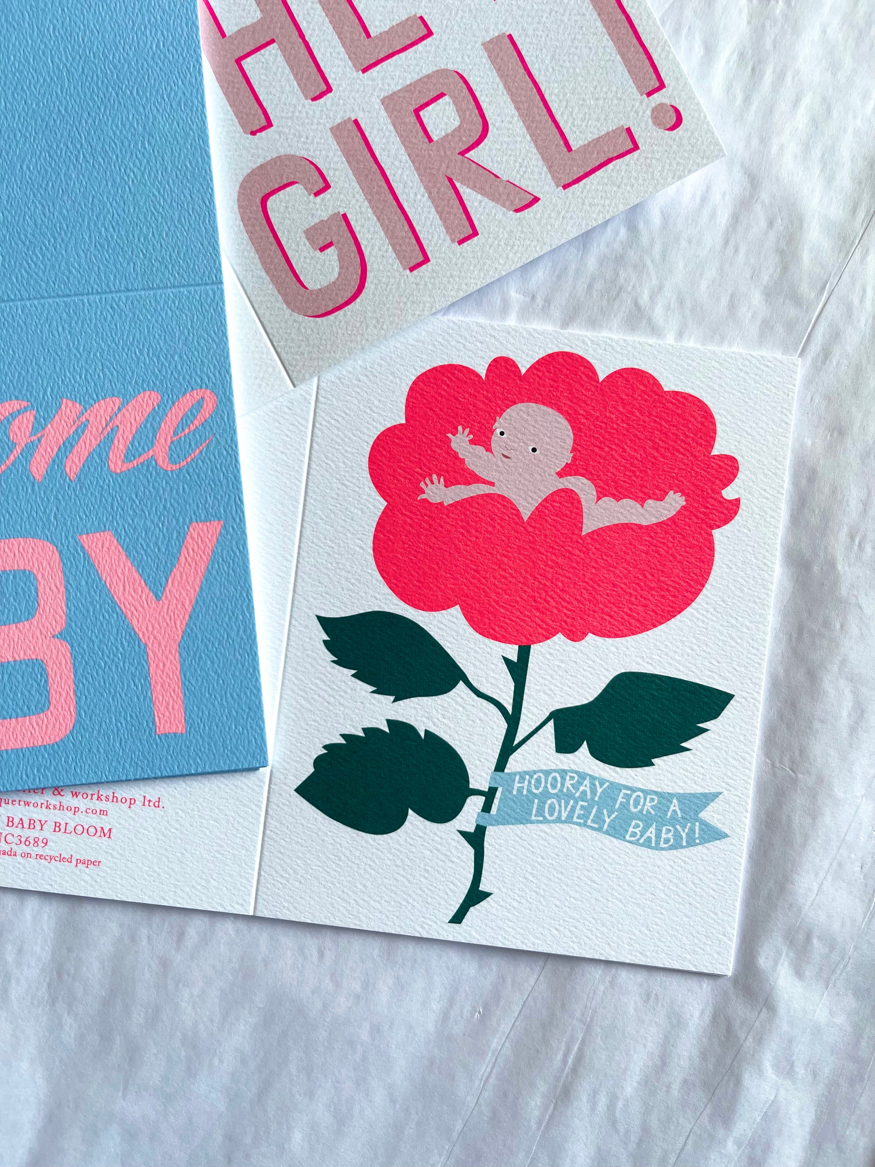 a cute new born baby inside a bring pink rose flower with green leaves and a blue banner that states Hooray for a Lovely Baby
