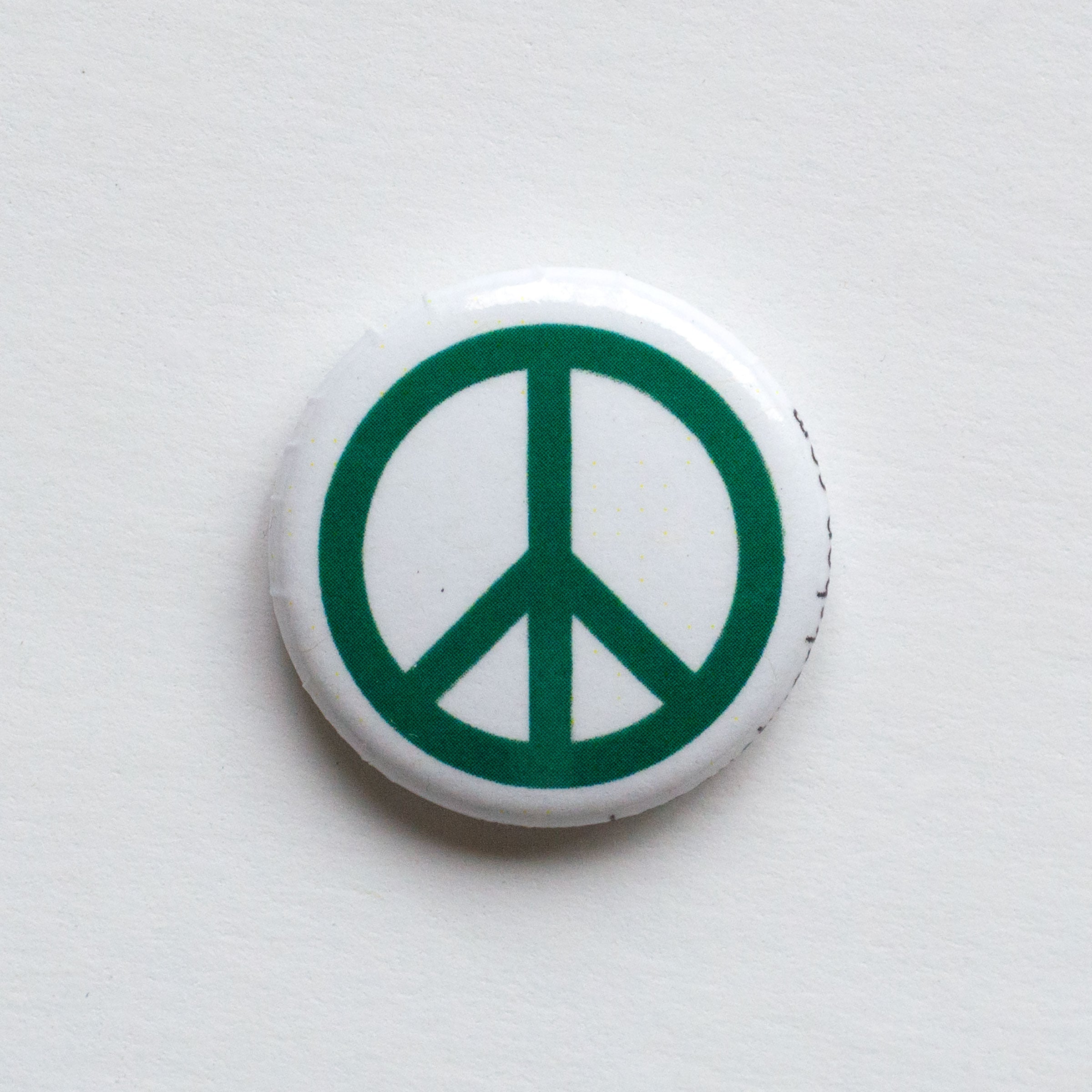 A pin with a green peace symbol on a white background.