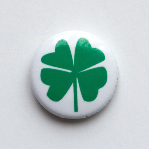 A green 4 leaf clover in a bright emerald green on a white background with a pin to fix to a jacket