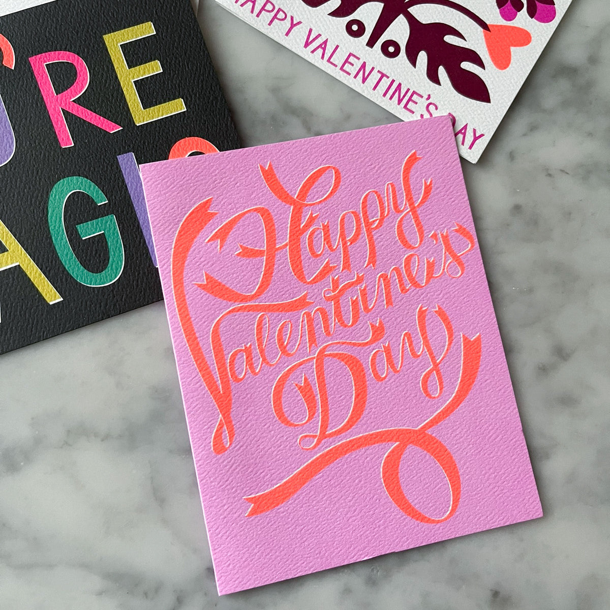 Pink card with 'Happy Valentine's Day' text on a marble surface
