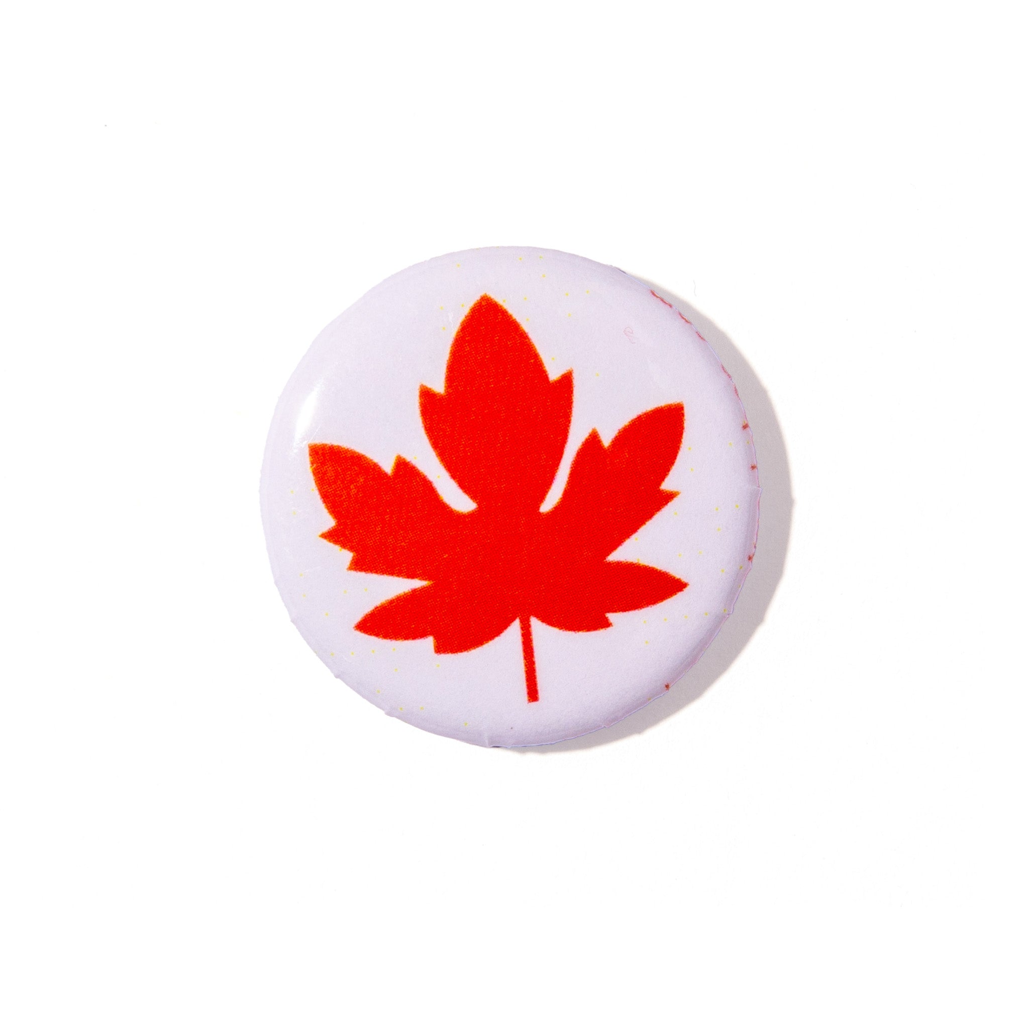 A round white button pin featuring a bold red maple leaf design, shown on a clean white background.