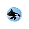 A round pinback button featuring a black and white orca design on a light blue background, shown on a plain white studio background.