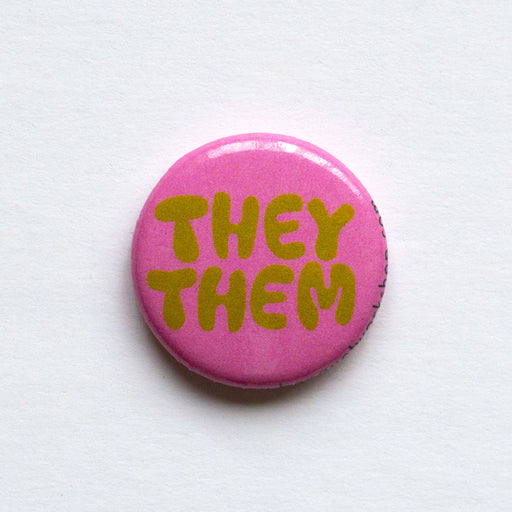 one inch lapel button reads "They Them" in funny mustard lettering on a rose pink