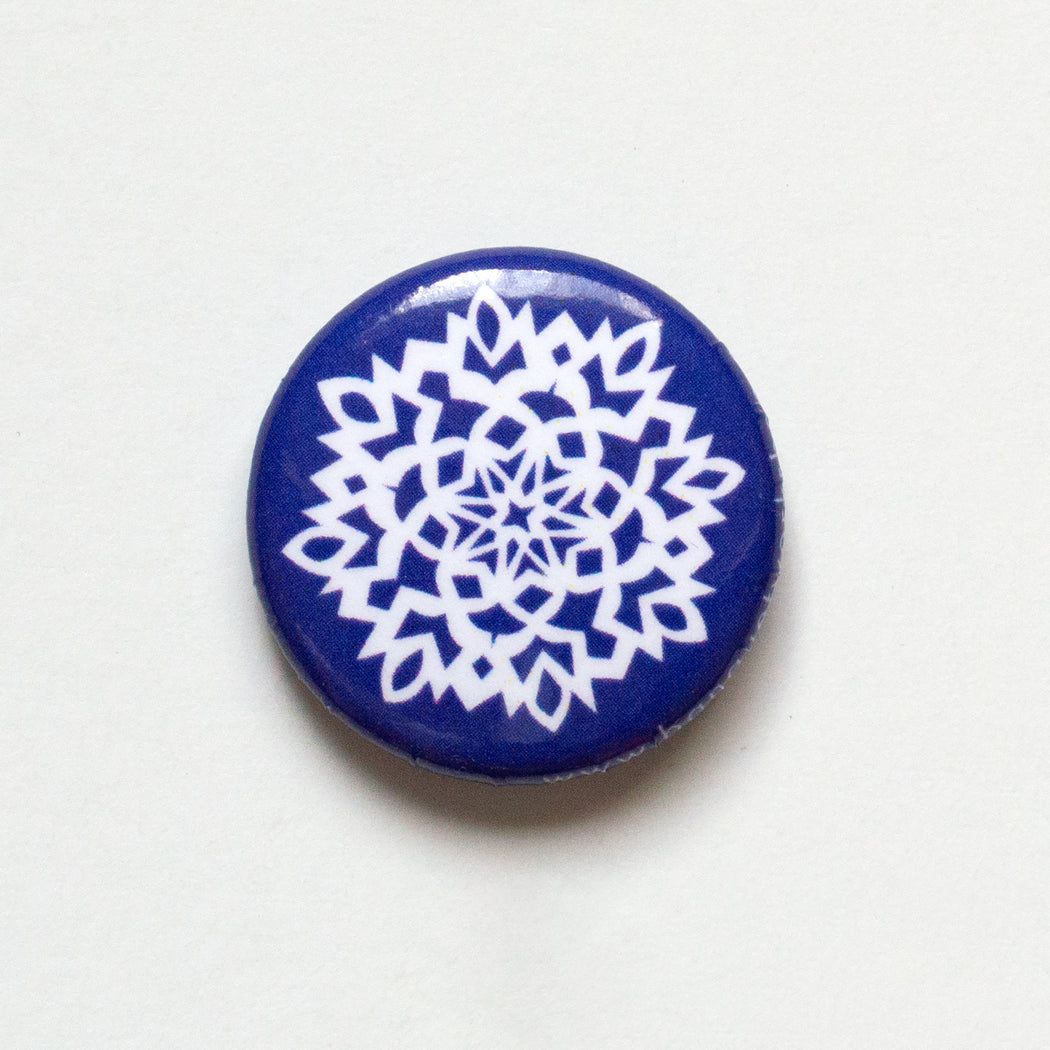 paper cut out snowflake in white on a blue 1" button