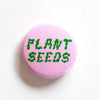 one inch button says plant seeds in wiggly  pink and green typeface