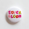 one inch button says "super bloom" in multicoloured lettering