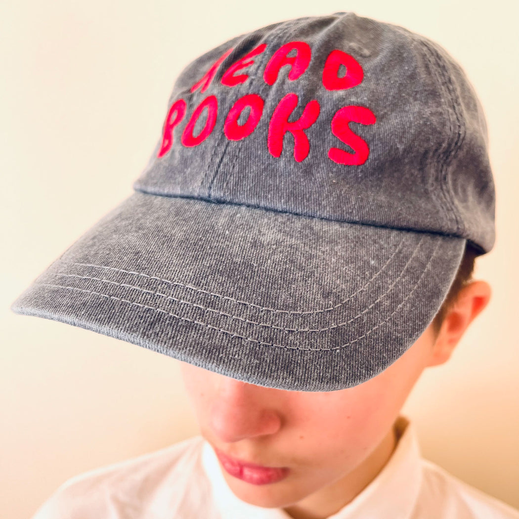 woman wearing a navy stonewashed cotton cap embroidered with the phrase READ BOOKS