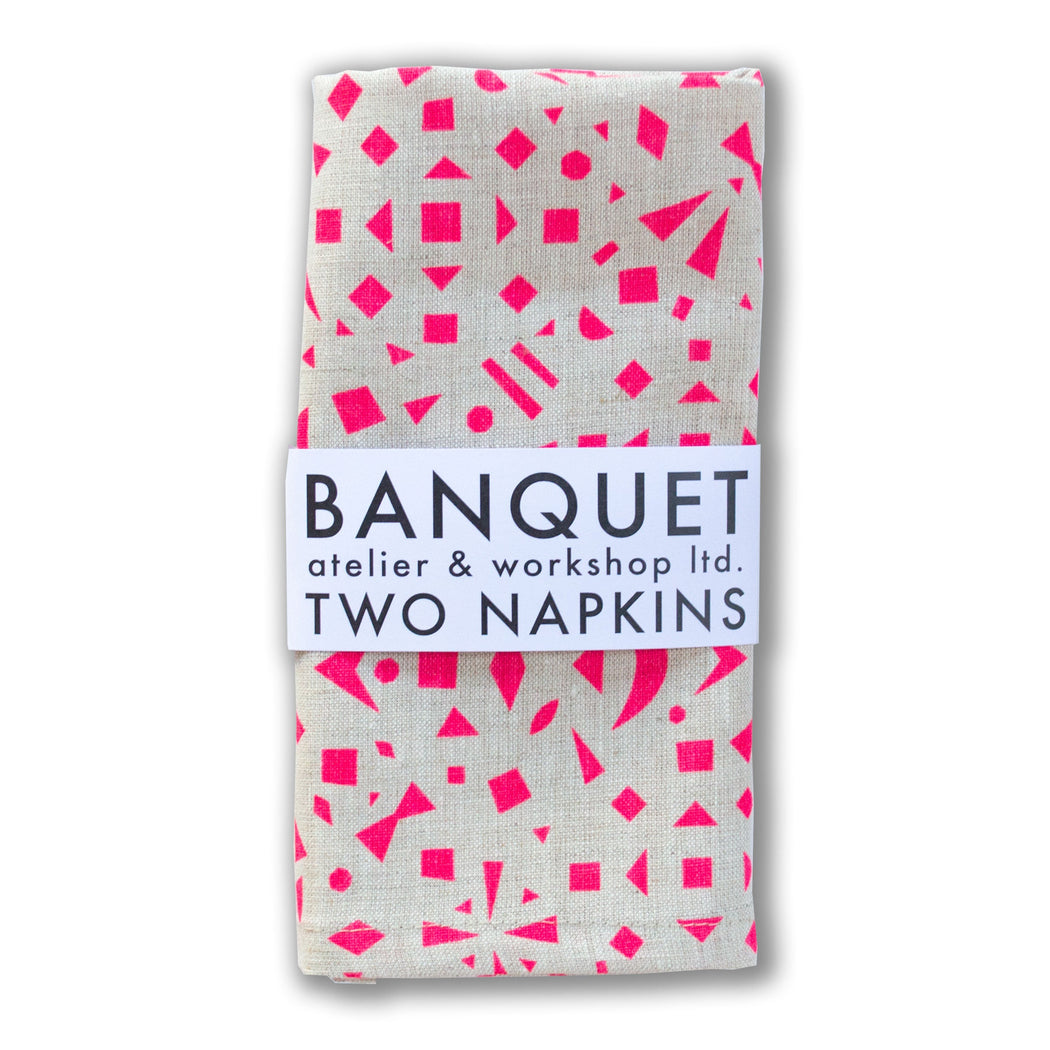 scattered neon pink shapes (triangles, squares, bow and trapezoids) on a pair of linen napkins