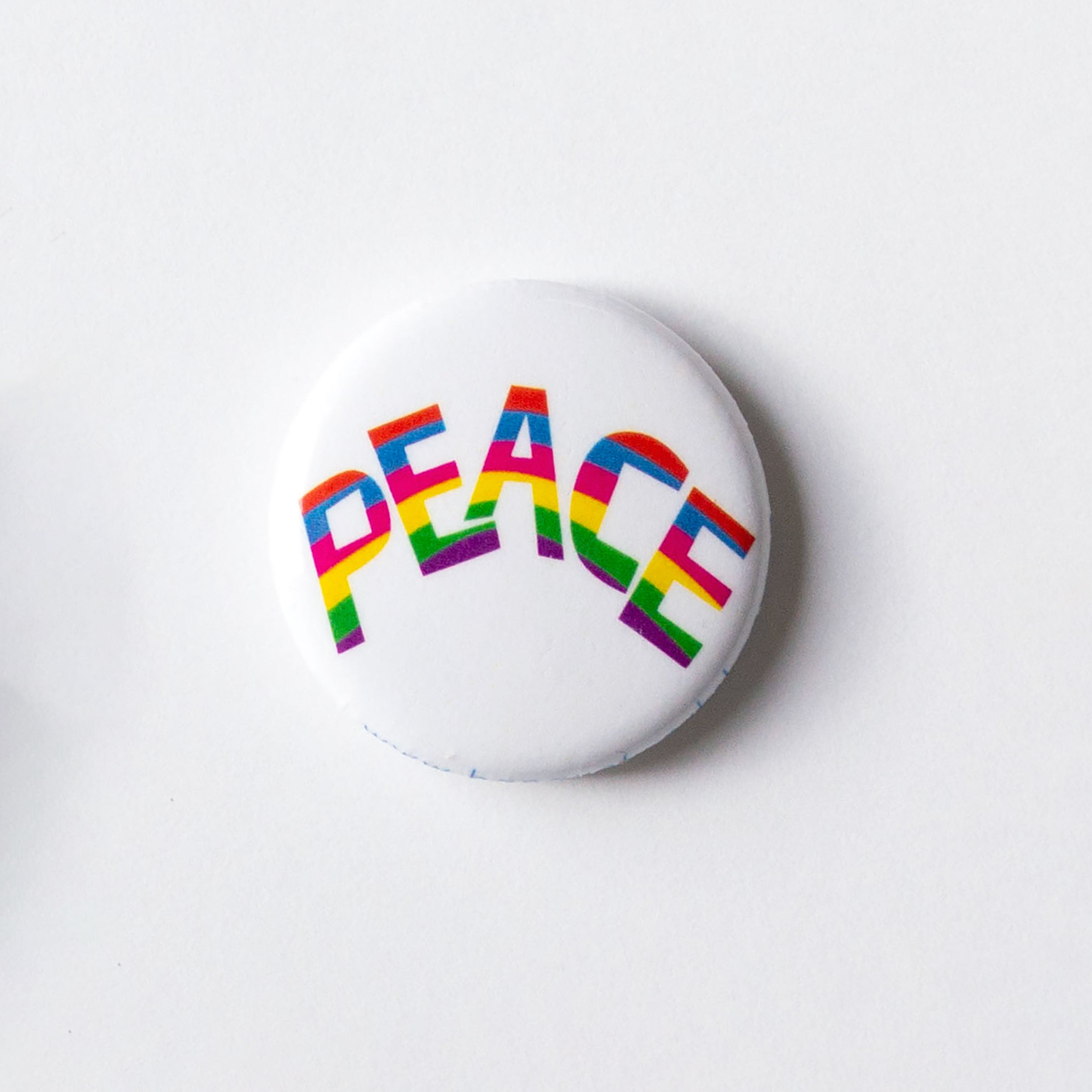 1 inch button with PEACE spelled out in rainbow letters