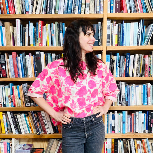 Woman wearing an oversized linen shirt in a natural colour with a bright neon pink rose pattern 
