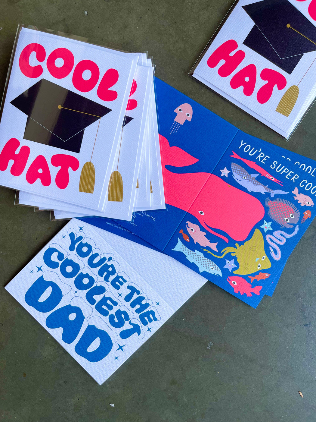 Note Card  that says You're Super Cool with multiple drawings of fish including Whale, Eel, Starfish and Manta Ray in bright colours including neon pink and lavender and light pink with a stack of Cool Hat graduation card with a hat with tassel