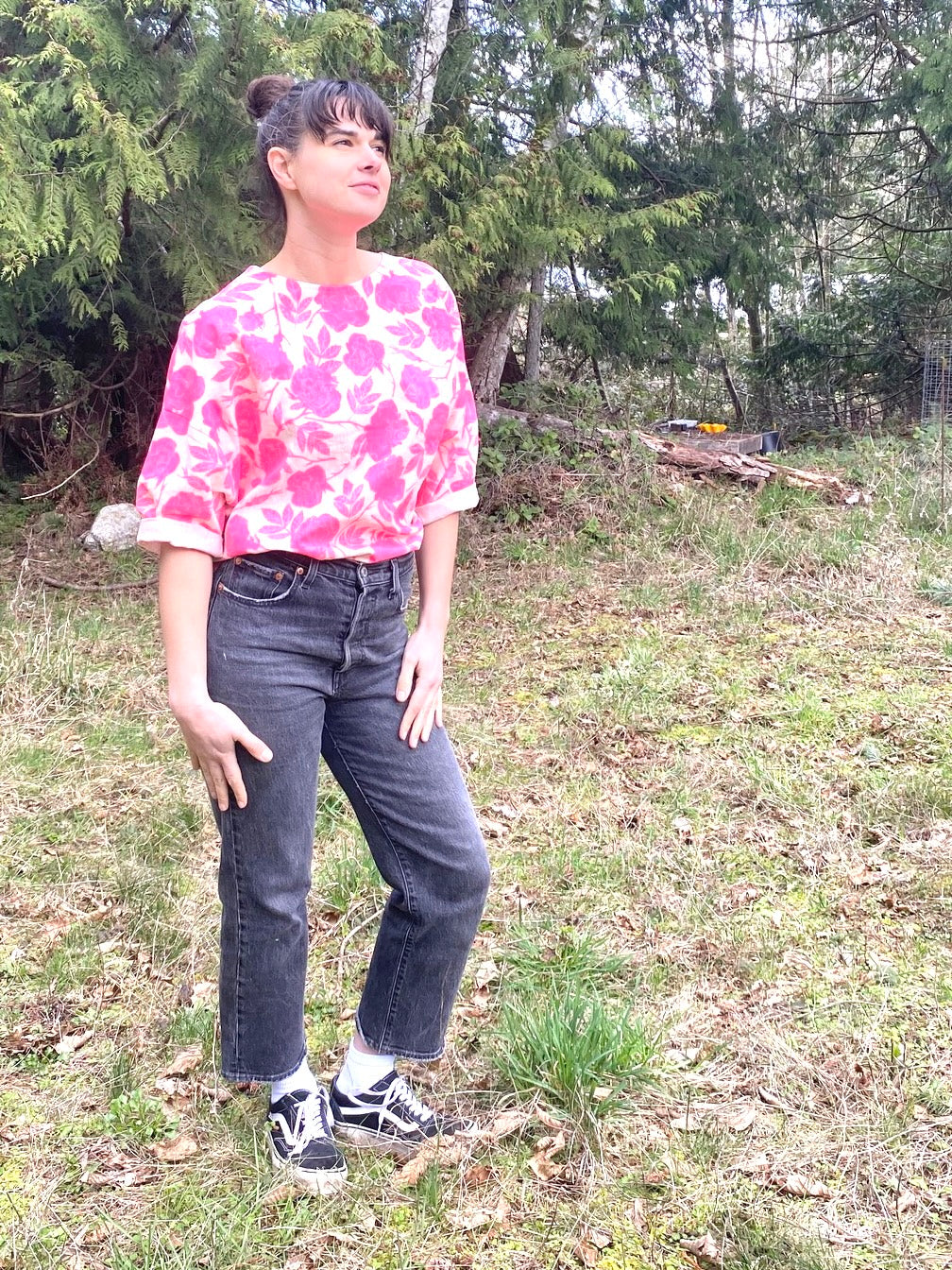 Woman wearing a neon pink rose patterned oversized linen shirt with rolled sleeves in front of trees