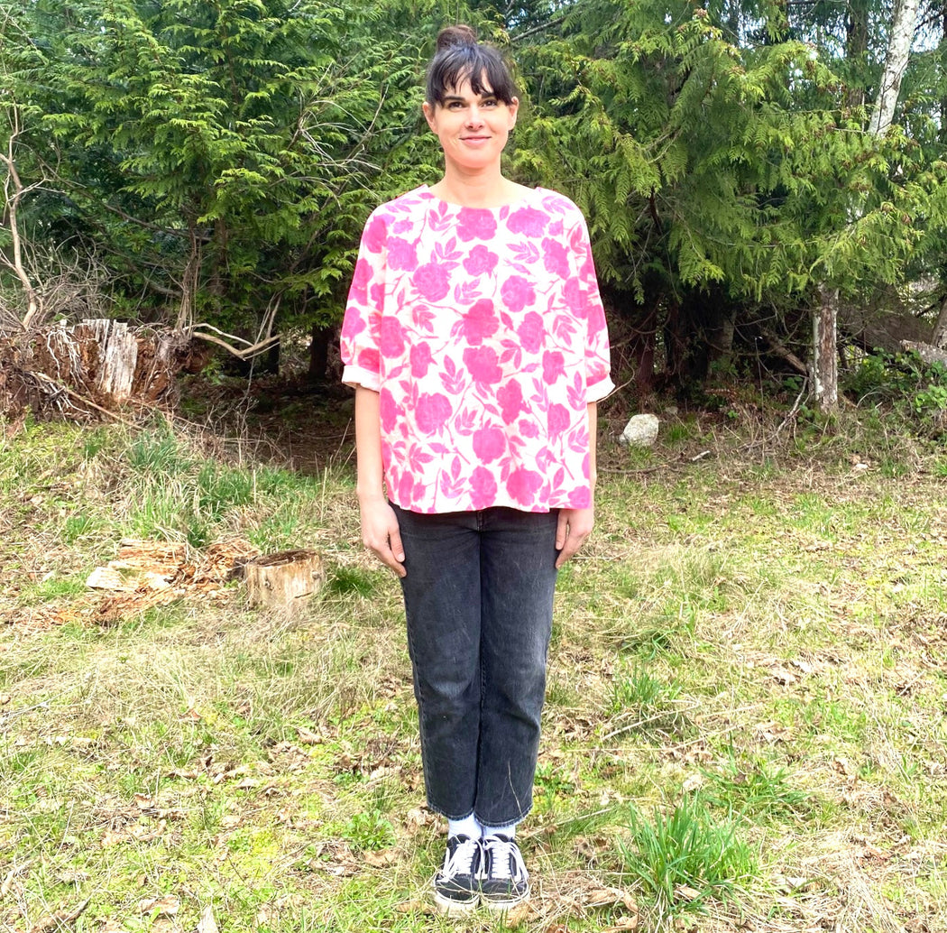 Women wearing a linen shirt with a neon pink rose pattern printed on it standing in front of trees