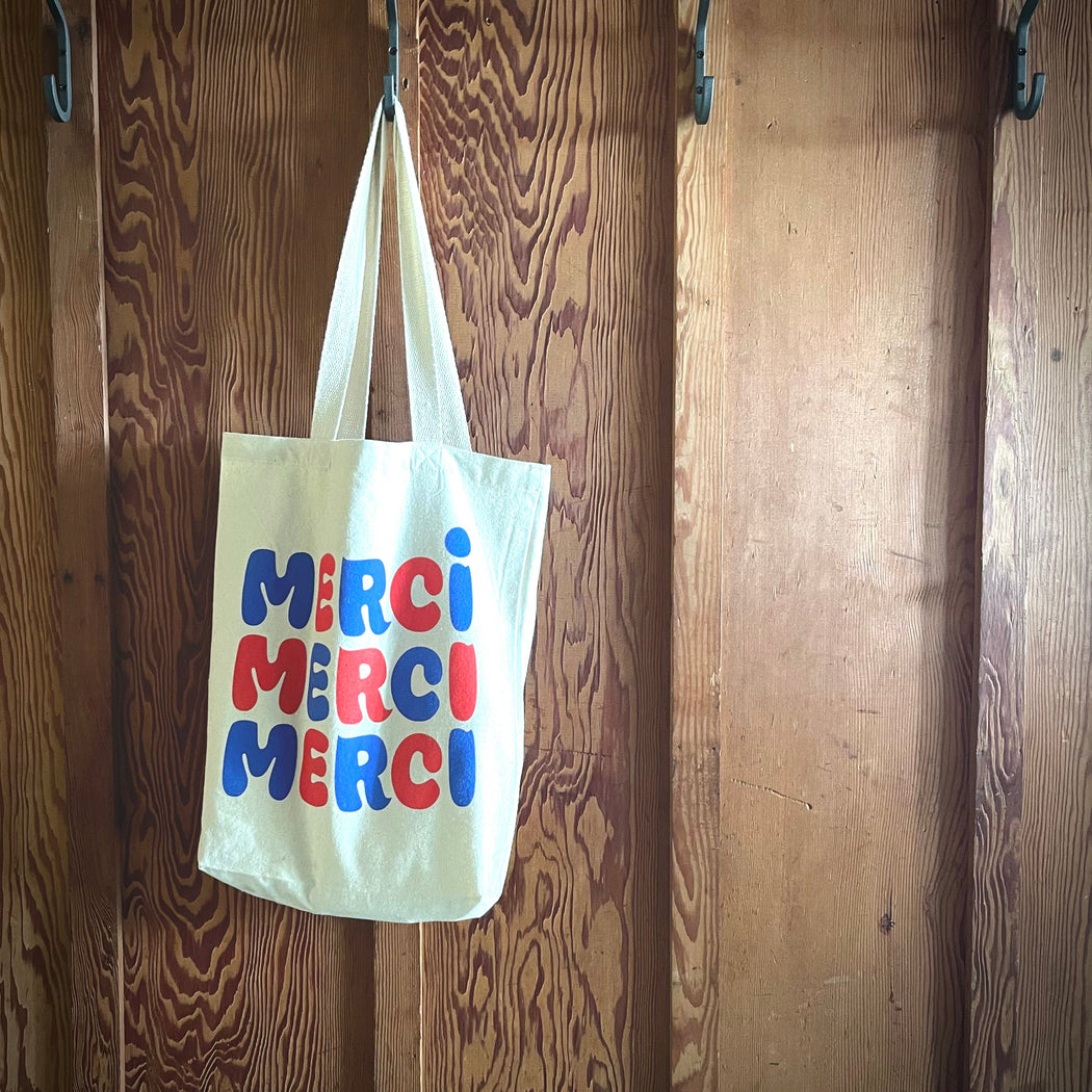 red and blue merci tote bag hanging on an old wood board and batten wall